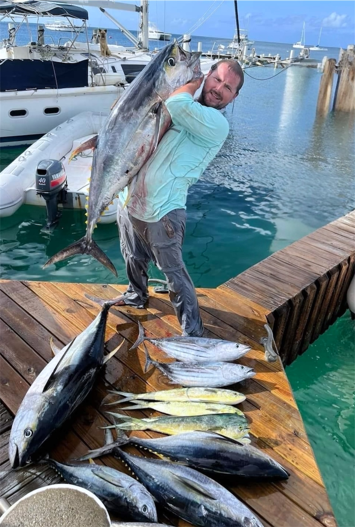 Angler shouldering a yellowfin tuna beside a full dock spread of the day's catch